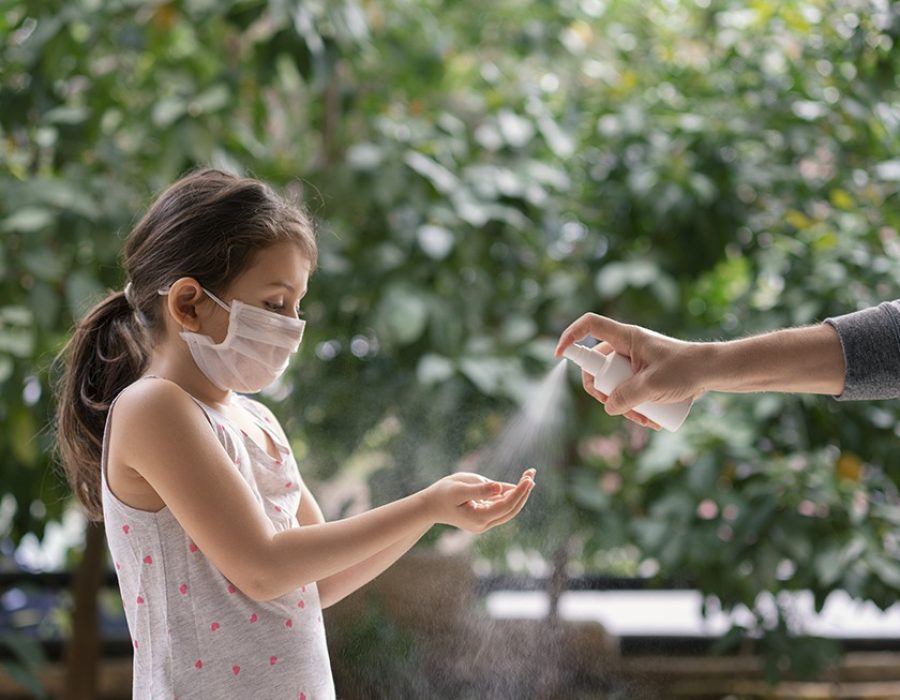 Father squirts antibacterial hand sanitizer in daughter's hands, Little girl wears a face mask during coronavirus and flu outbreak