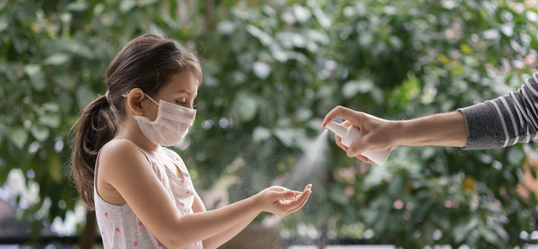Father squirts antibacterial hand sanitizer in daughter's hands, Little girl wears a face mask during coronavirus and flu outbreak