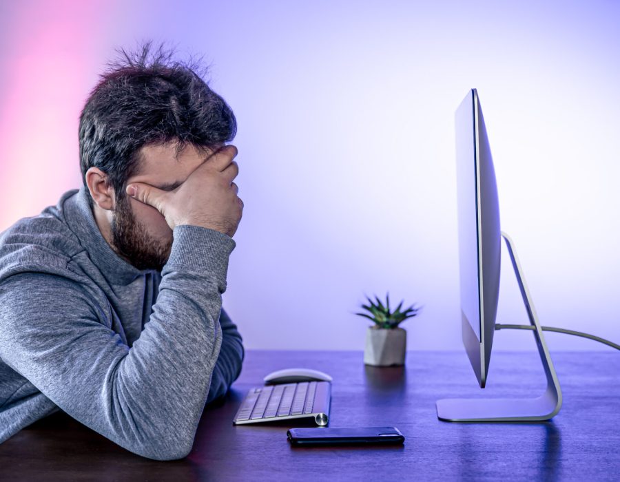 Tired man sits in front of the computer, covered his face with his hands, office work, night work, burnout at work.